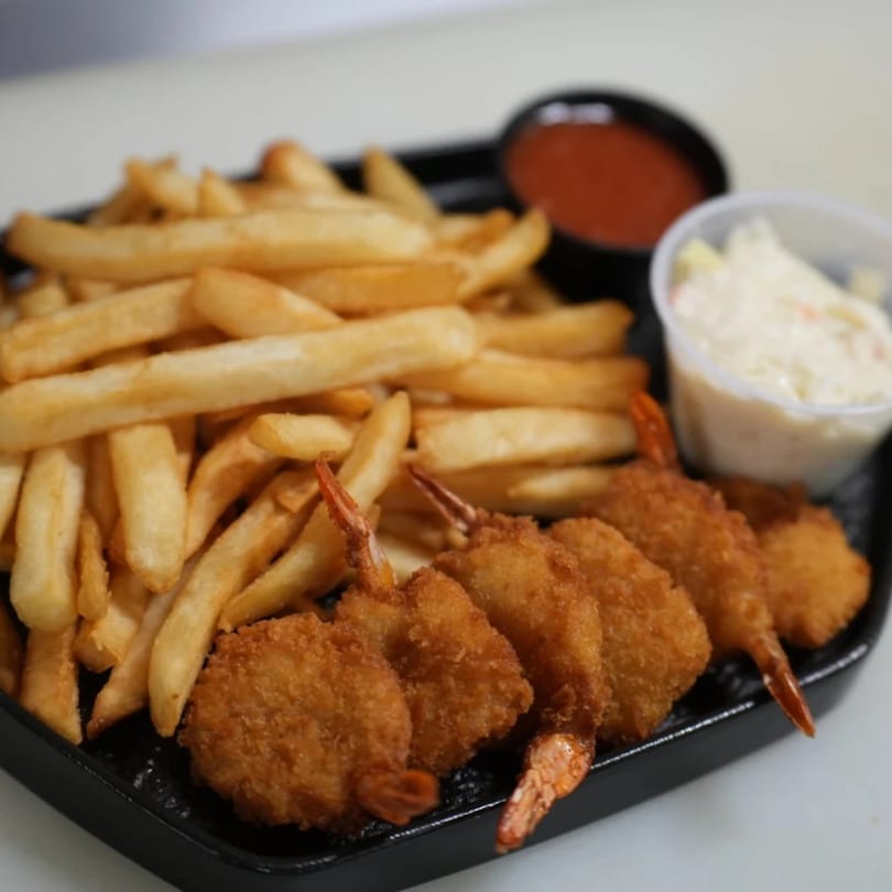 A black tray holds golden french fries, crispy breaded shrimp, ketchup, and tartar sauce.