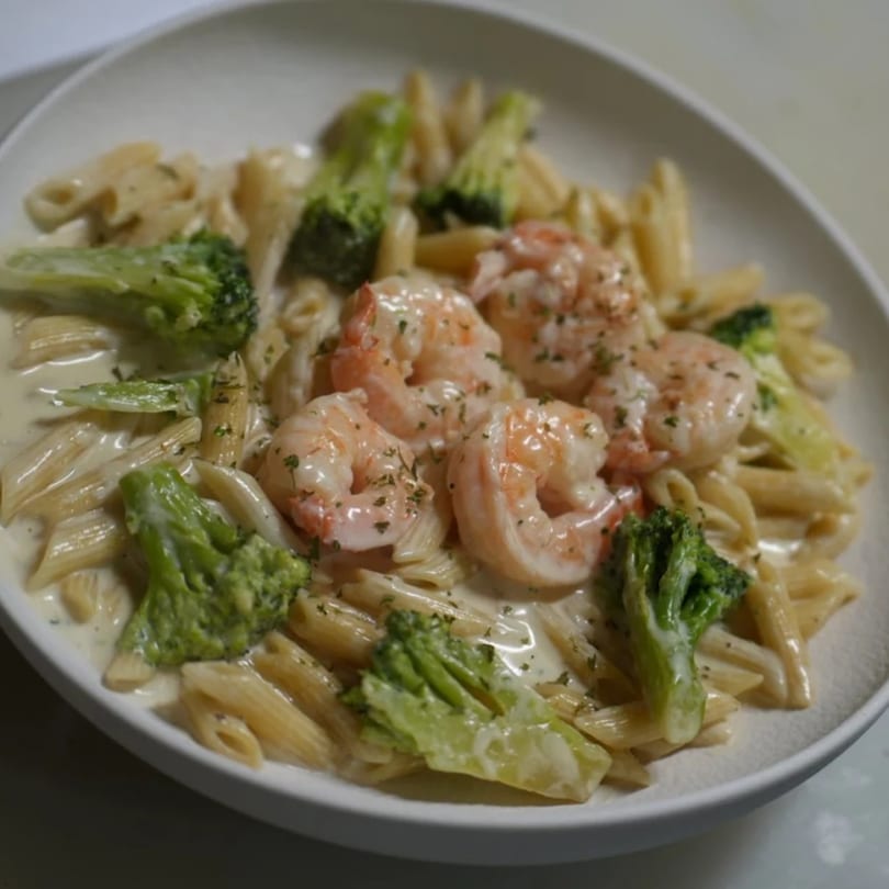 Penne pasta with creamy sauce, shrimp, and broccoli florets, garnished with herbs.