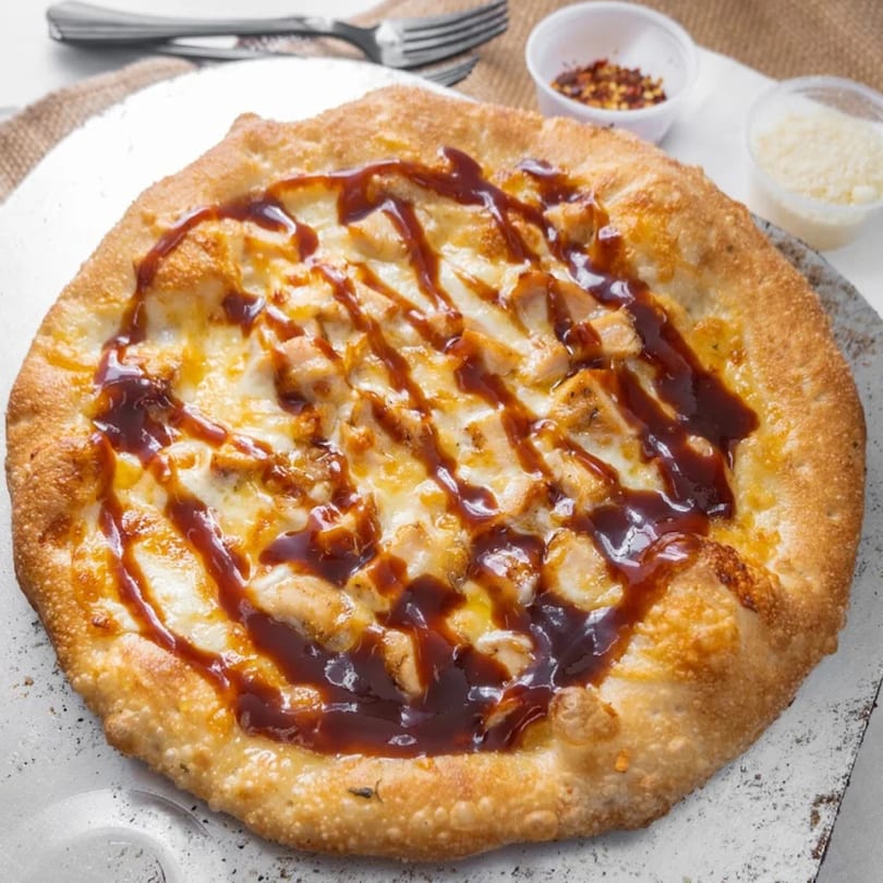 Vito's BBQ chicken pizza with melted cheese and a crispy crust, alongside red pepper flakes and parmesan.