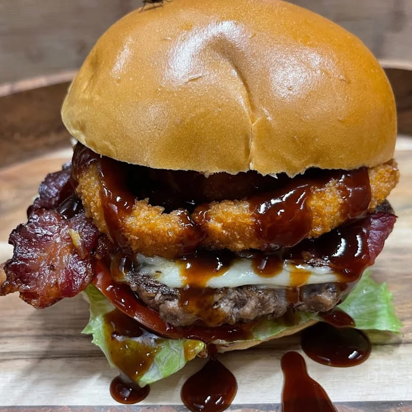 A juicy burger from Vito's with bacon, cheese, onion rings, and BBQ sauce dripping down.